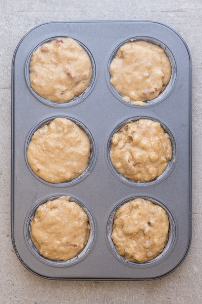 adding the pumpkin muffin mixture to the prepared muffin pan.