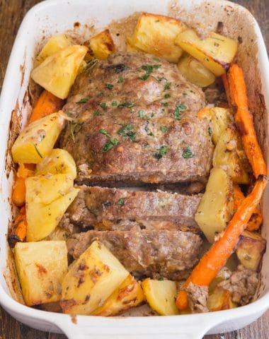 stuffed meatloaf in a white pan with potatoes and carrots