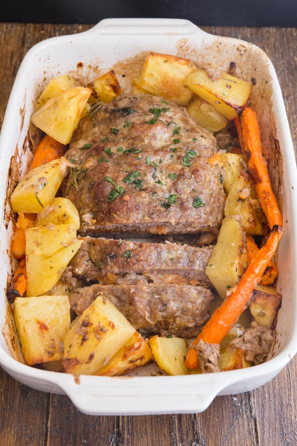 stuffed meatloaf in a white pan with potatoes and carrots