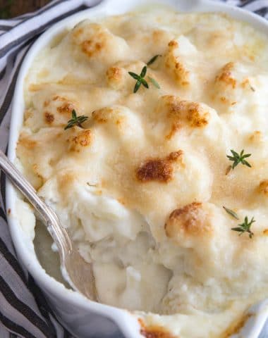 cauliflower casserole in a white baking dish with fresh thyme on top