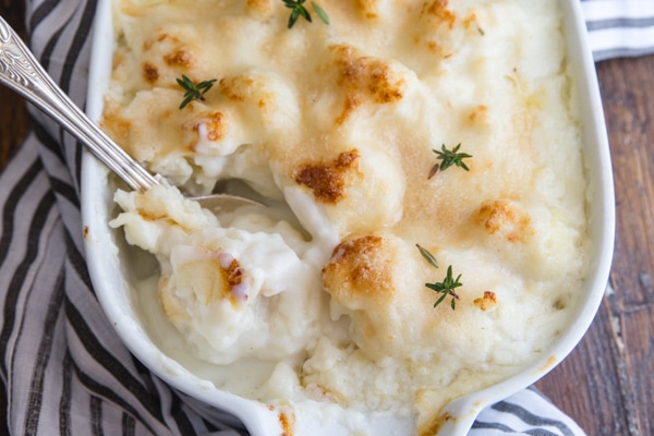up close cauliflower casserole with a spoonful in a white baking pan