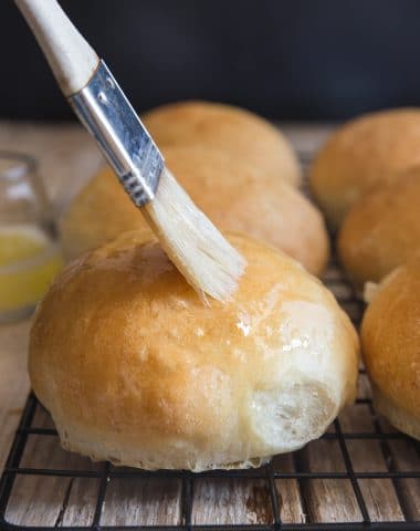 dinner rolls on a wire rack brushing with melted butter