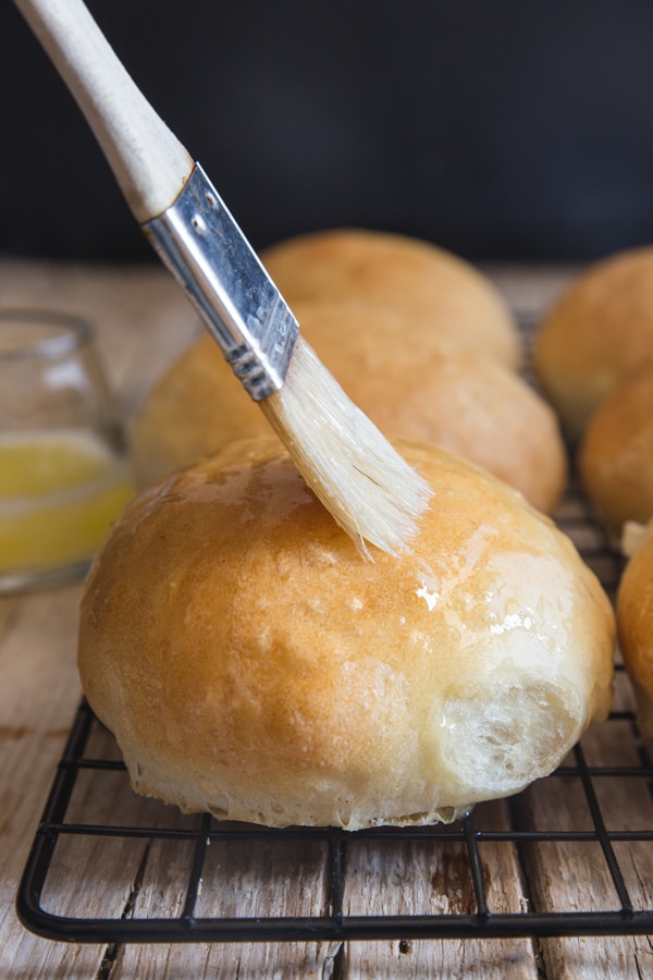 dinner rolls on a wire rack brushing with melted butter
