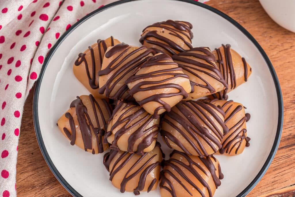 Chocolate drizzled caramels on a white plate.