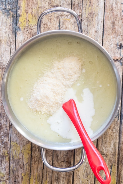 adding the cream and parmesan cheese to the blended cauliflower soup