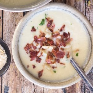 cauliflower soup in a white bowl with chopped bacon and parsley