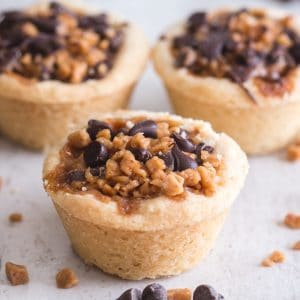3 cookie cups on a white board with chips and toffee bits sprinkled