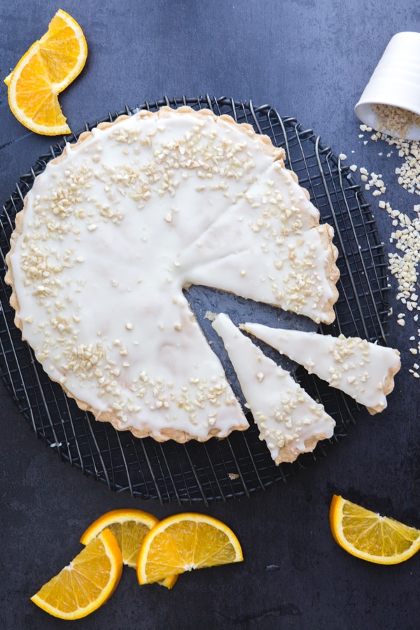 orange shortbread on a black wire rack with 2 pieces cut and orange slices around it