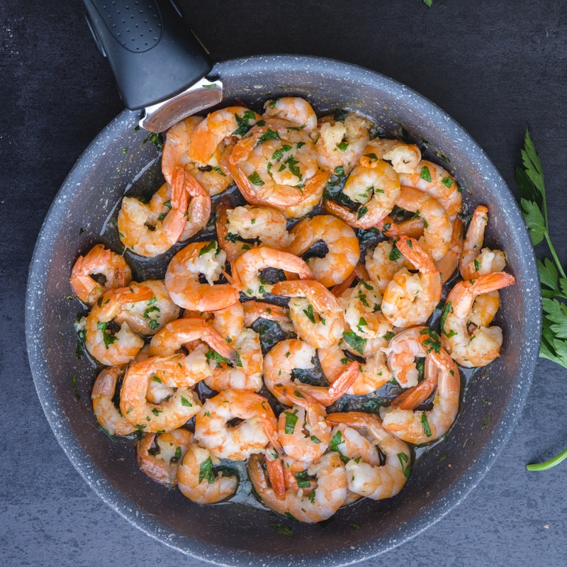 sauteed shrimp with parsley in a black frying pan