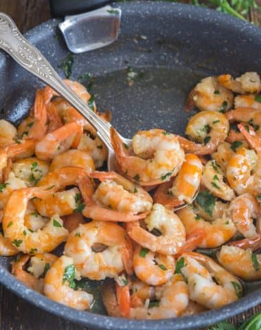 sauteed shrimp with parsley in a black frying pan and a silver spoon