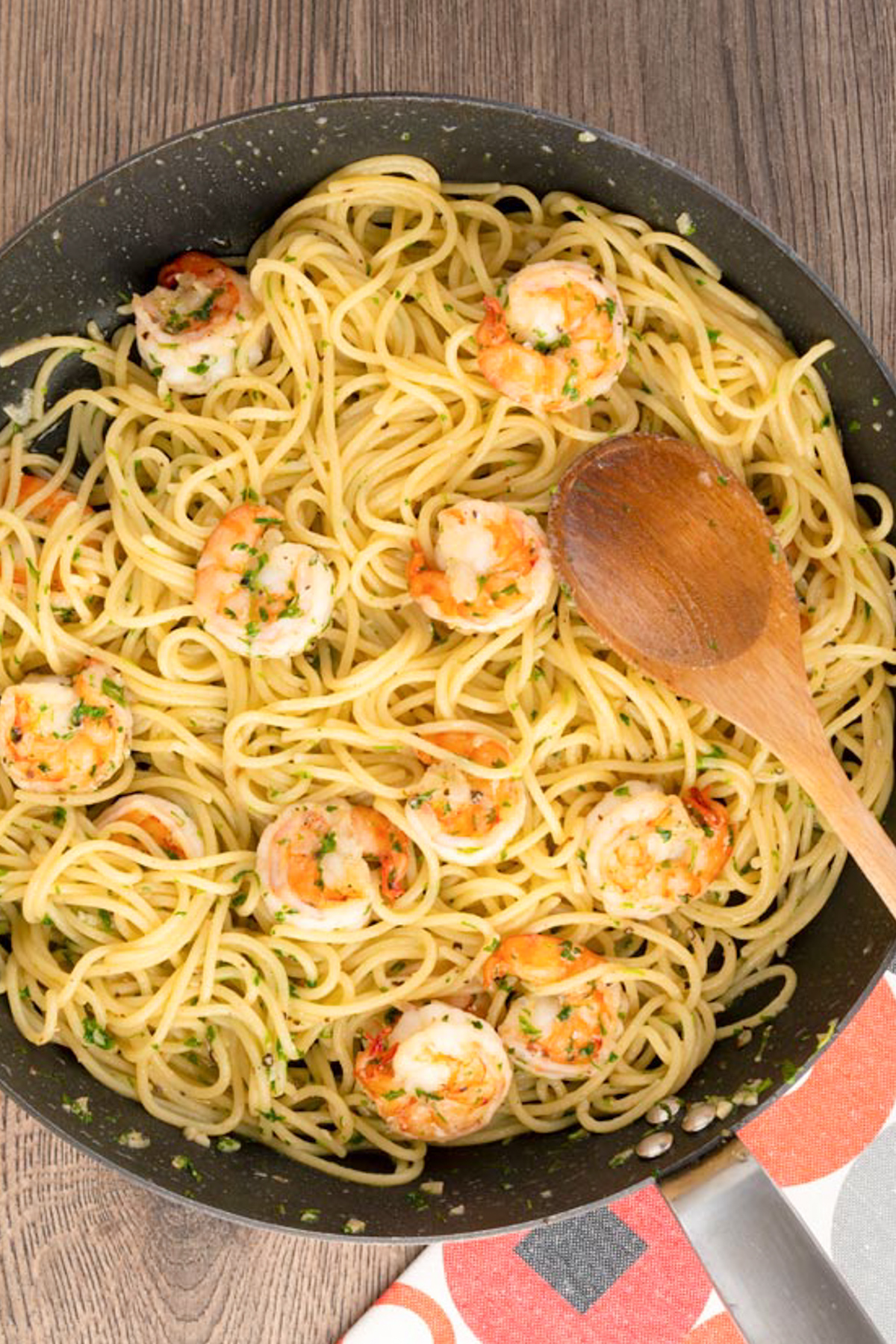 Shrimp pasta in a black pan with a wooden spoon.