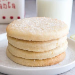 4 lemon sugar cookies on a white plate with a glass of milk and milk jar in the back