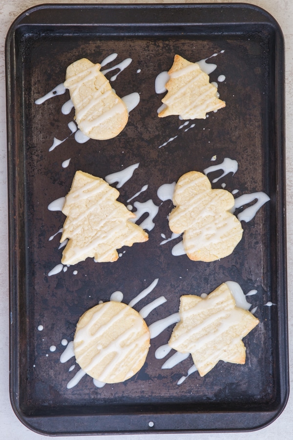 sugar cookies baked drizzled with lemon glaze on a black cookie sheet