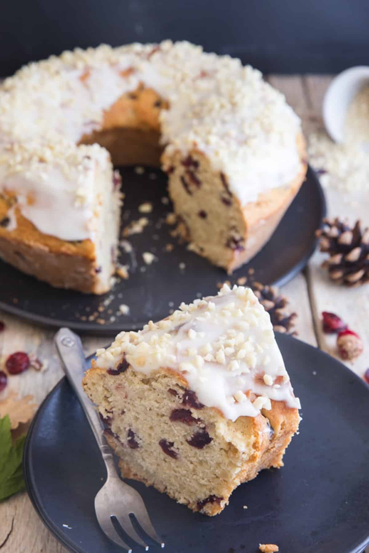 Cranberry cake on black cake stand and a slice on a black plate with a fork.