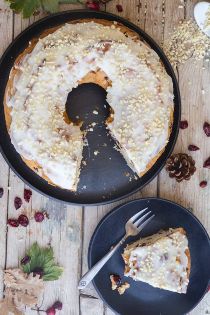 Cranberry cake on black cake stand and a slice on a black plate with a fork.