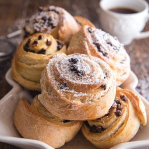 sweet buns on a white christmas tree plate with a cup of coffee and powdered sugar sifter