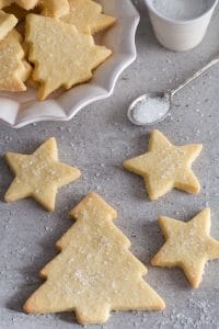 one tree and 3 stars with some cookies on a plate and a spoon of sparkling sugar on a grey board