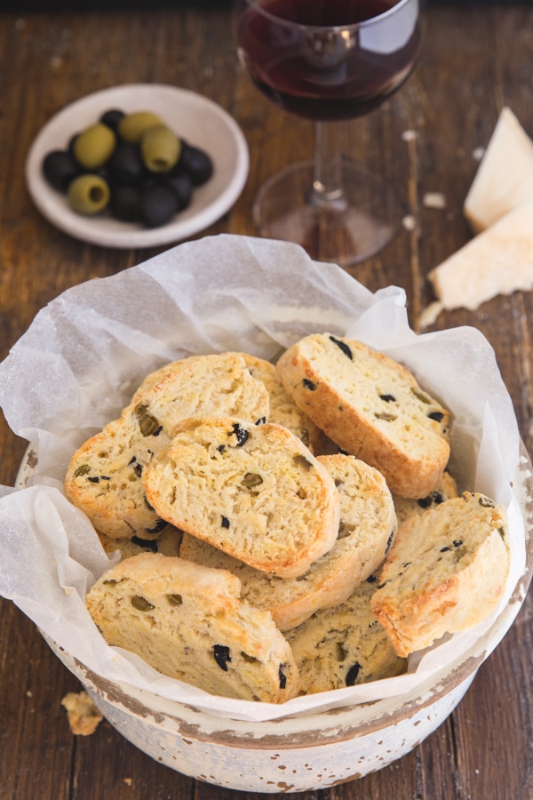 savory biscotti in a bowl with olives in a small plate and a glass of red wine