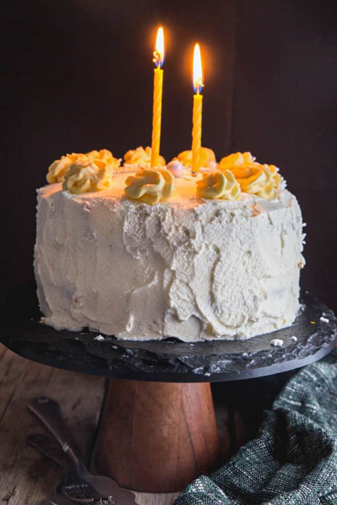 Birthday cake on a black cake stand with two lit candles.