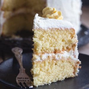 a slice of vanilla cake with lemon mascarpone icing on a black plate