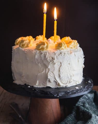 birthday cake on a black cake stand with two lit candles