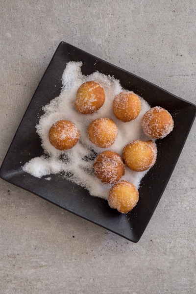 castagnole fried and rolling in sugar on a black plate