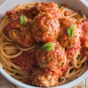 3 meatballs on a bowl of spaghetti with basil leaves on top