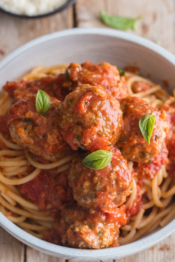 3 meatballs on a bowl of spaghetti with basil leaves on top
