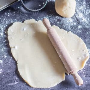 Pie dough with a rolling pin on a blue board.
