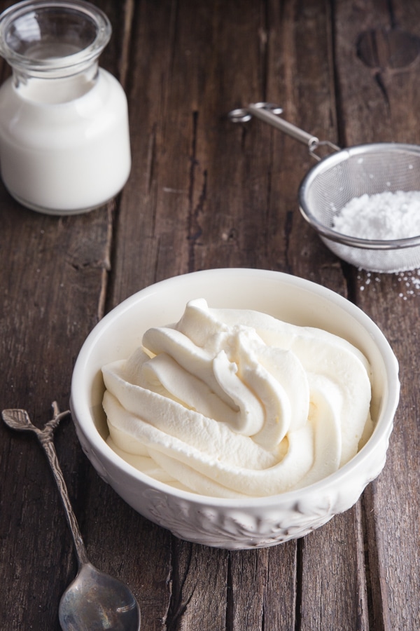 mascarpone cream in a white bowl with cream in a small glass jar and powdered sugar in a sifter