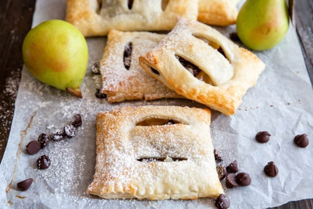Pastries on parchment paper with chocolate chips and 2 pears.