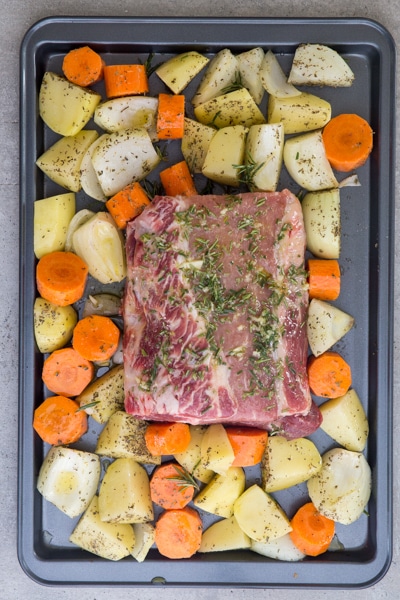 roast and vegetables on a black cookie sheet ready for baking