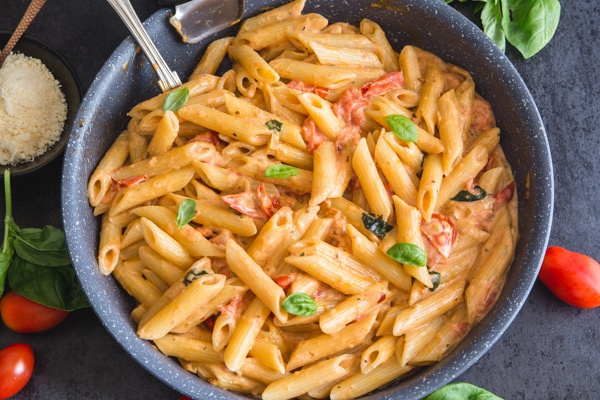 tomato pasta in a black pan with parmesan cheese in a bowl and fresh tomatoes