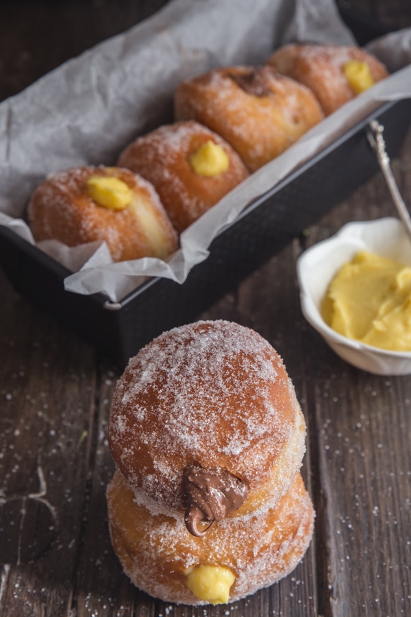 bomboloni in a loaf pan and 2 on top of each other with pastry cream in a white bowl with a spoon