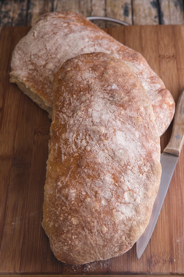 2 ciabatta loaves on a wooden board with a knife