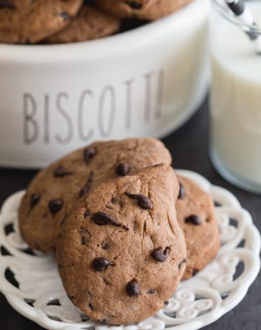 gocciole on a small plate with a glass of milk and a black and white straw and cookies in a biscotti container