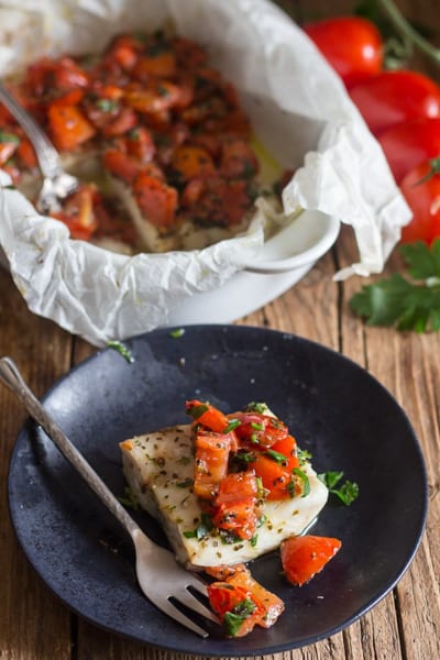 Baked fish marinara on a black plate.