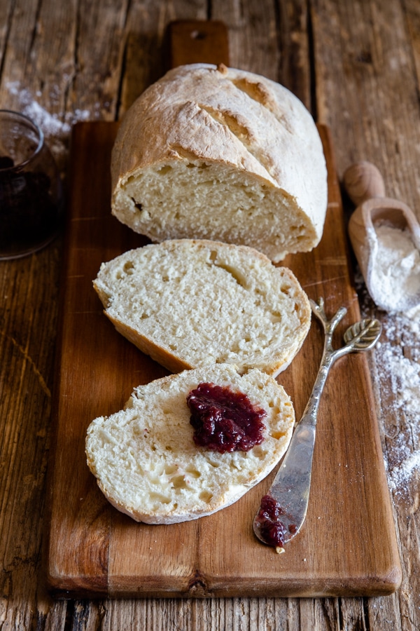 loaf of bread with 2 slices and some jam on a slice with a knife