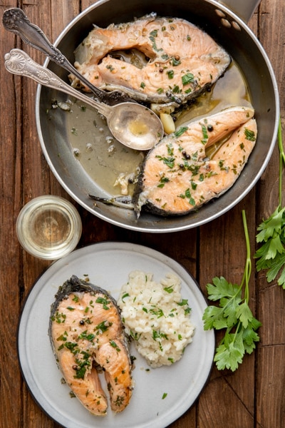 2 salmon steaks in a black pan and 1 on a white plate.