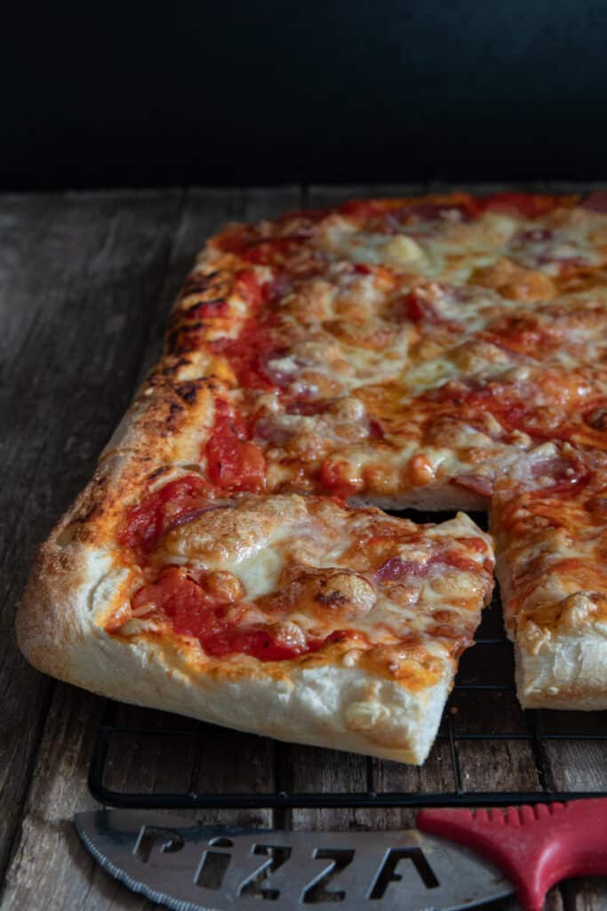 Pizza on a wire rack with a slice cut.