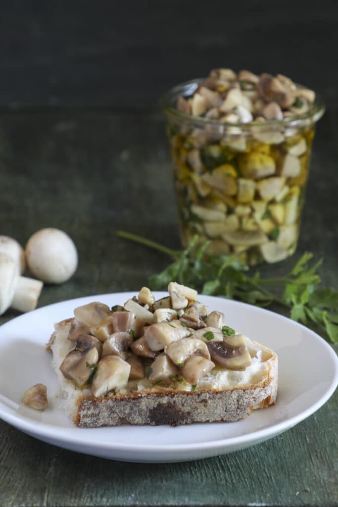 Mushrooms in a jar and some on a piece of bread on a white plate.