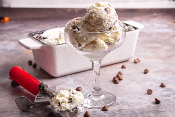 ice cream in the loaf pan with a scoop and 3 scoops in a tall glass dish