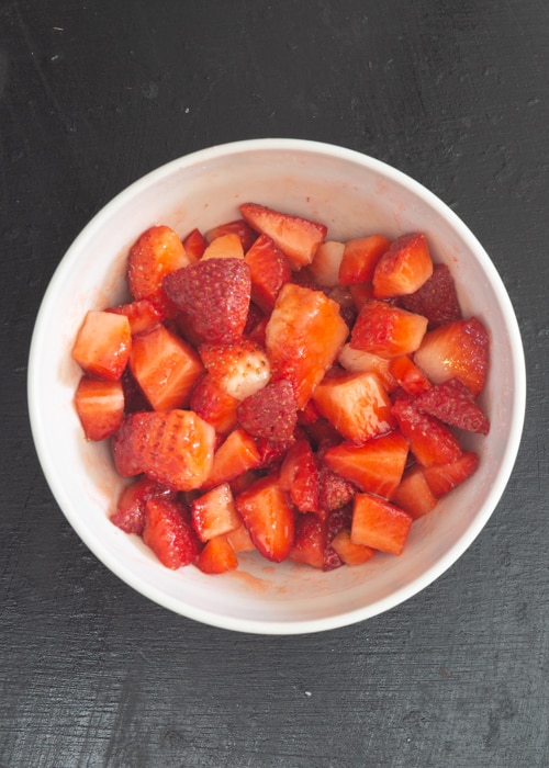 The chopped strawberries in a white bowl.