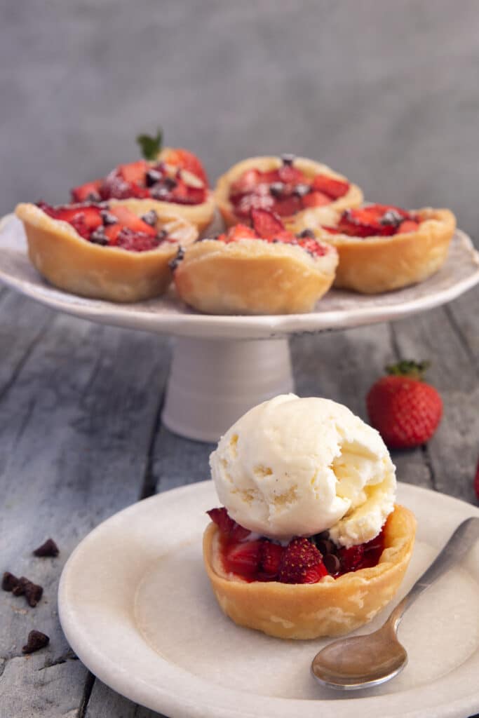 Tarts on a white cake stand with one with a scoop of ice cream on a white plate with a spoon.