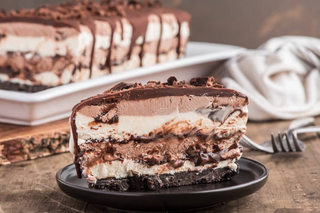 Ice cream cake on a white plate with a slice on a black plate.