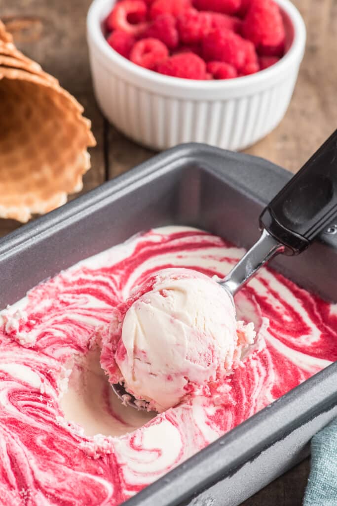 Raspberry ice cream in the loaf pan with a scoop.