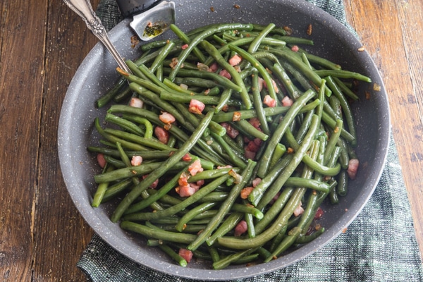 green beans & pancetta in a frying pan on a wooden board with a silver fork