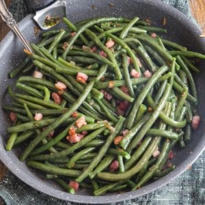green beans & pancetta in a frying pan on a wooden board with a spoon