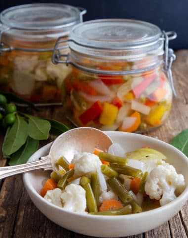 vegetables in a white bowl with a silver spoon and 2 jars full