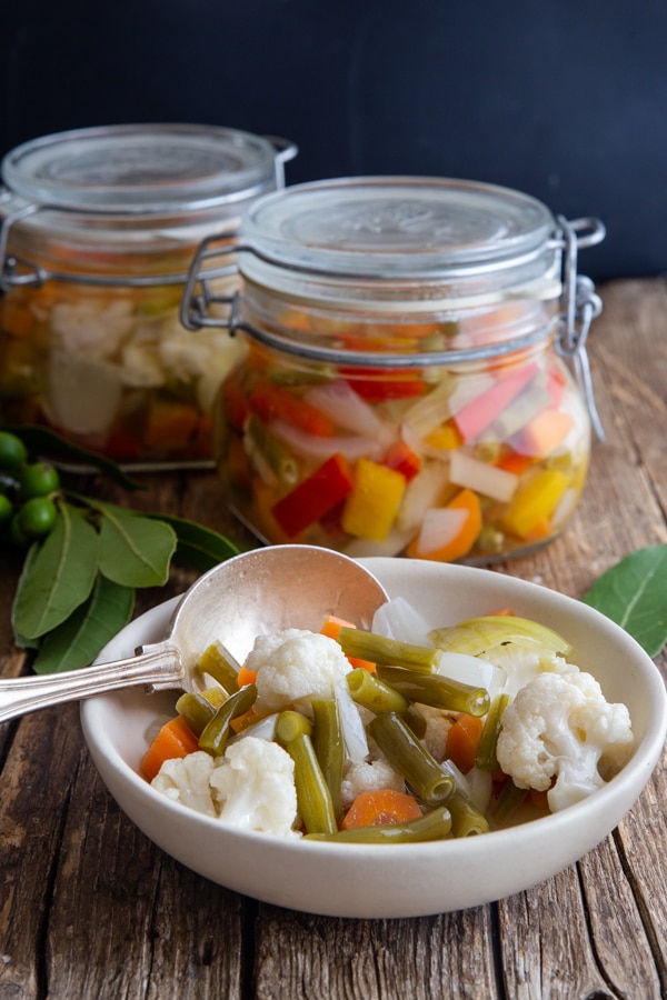 vegetables in a white bowl with a silver spoon and 2 jars full